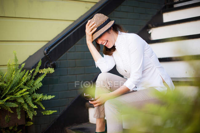 Femme adulte moyenne assise sur un escalier et riant — Photo de stock