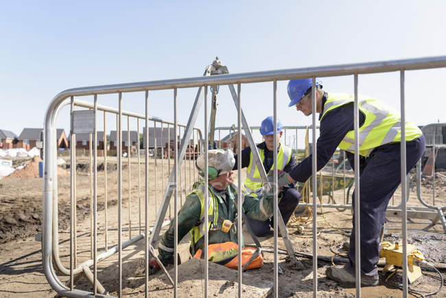 Apprentice builders assisting worker out of manhole on building site — Stock Photo