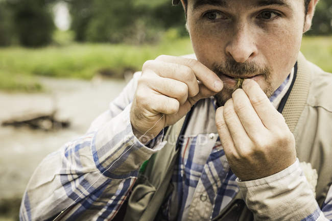 Cropped view of man biting fishing line looking away — Stock Photo