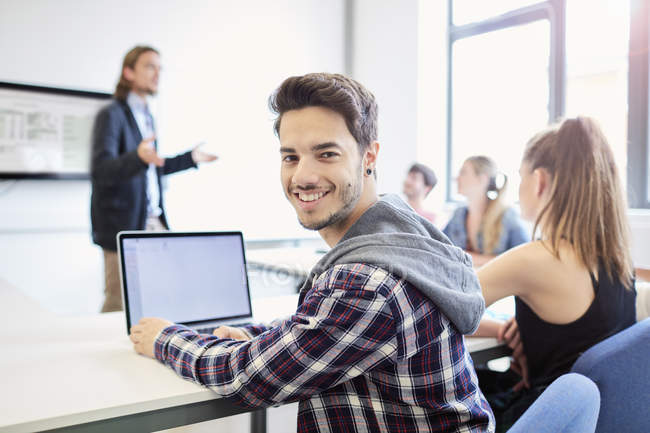 Portrait of young male student using laptop in higher education college classroom — Stock Photo