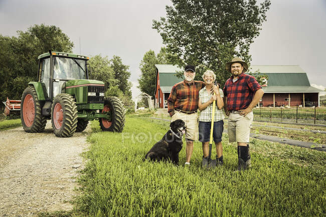 Família com cão na fazenda na frente do trator olhando para a câmera sorrindo — Fotografia de Stock