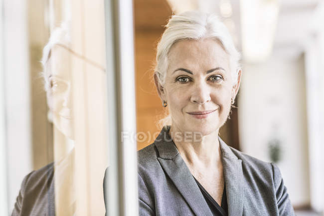 Бізнес-леді притулившись скляні двері, дивлячись на камеру посміхається — стокове фото