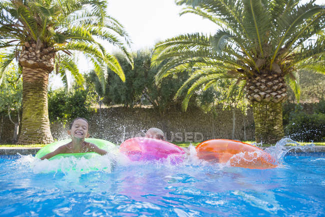 Tres niños salpicando en anillos inflables en la piscina del jardín - foto de stock