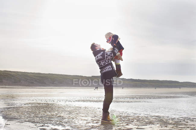 Взрослый мужчина поднимает дочь на пляж, Блумендал-ан-Зи, Нидерланды — стоковое фото
