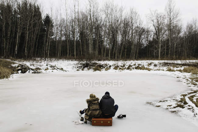 Coppia seduta su valigia rossa in mezzo al lago ghiacciato, Whitby, Ontario, Canada — Foto stock
