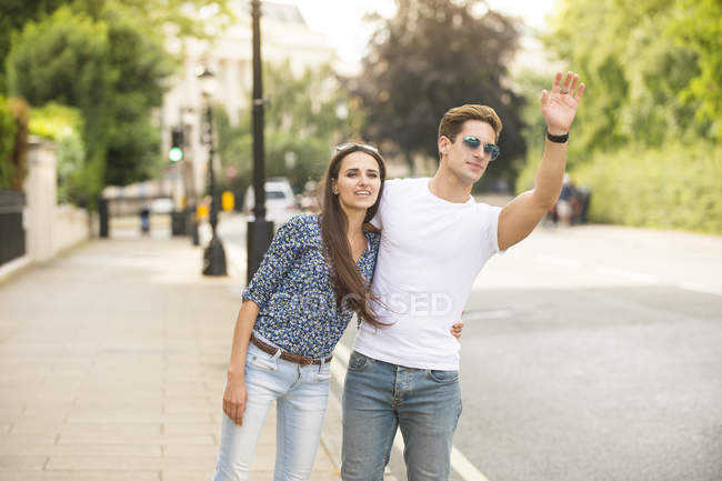 Young couple hailing a cab on city street, London, UK — Stock Photo