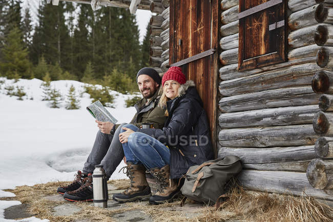 Portrait of couple reading map sitting outside log cabin in winter, Elmau, Bavaria, Germany — Stock Photo