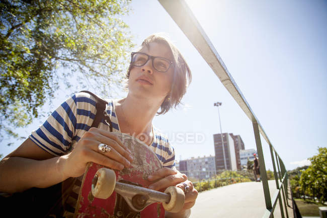 Young man holding skateboard, low angle view — Stock Photo