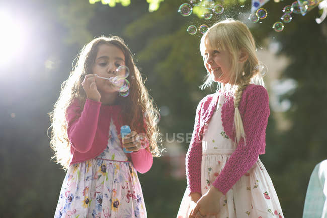 Две милые девушки дуют пузырьки в солнечном саду — стоковое фото