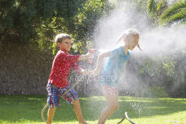 Хлопчик бризкає дівчину в саду з водою спринклер — стокове фото