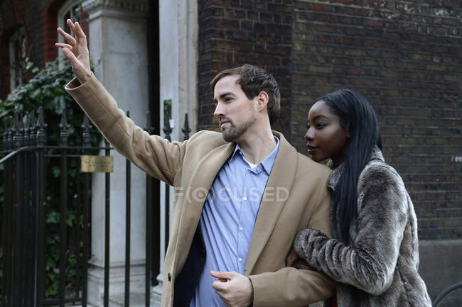 Couple outdoors, arm in arm, man hailing taxi — Stock Photo