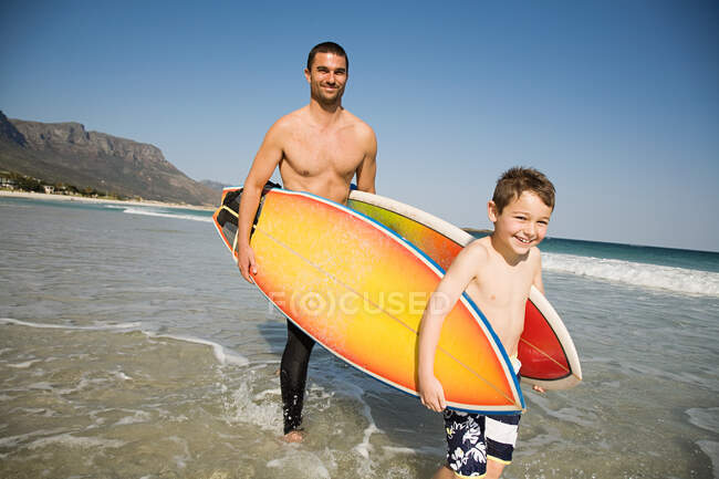 Father and son carrying surfboards in from the sea — Stock Photo