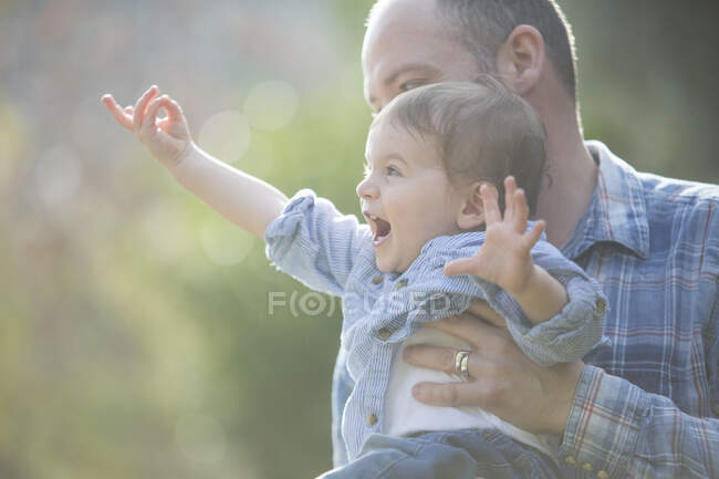 Vista lateral del niño siendo sostenido por el padre, señalando con entusiasmo - foto de stock