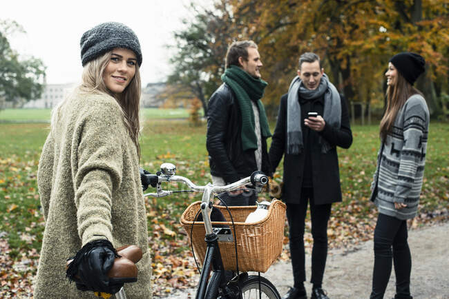 Giovane donna con bici, amici in background — Foto stock