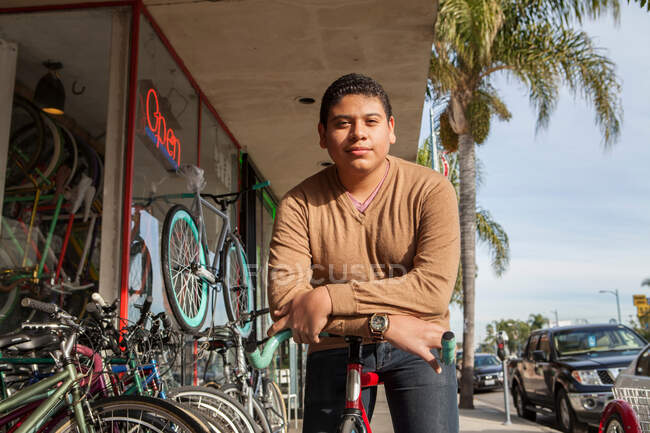 Junge stützt sich vor Geschäft auf Fahrrad — Stockfoto