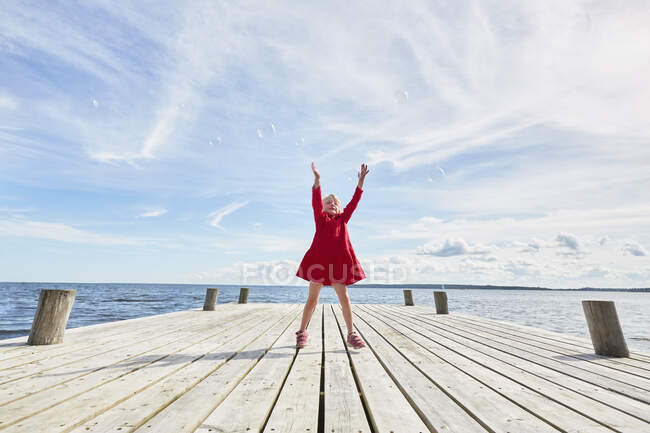 Молода дівчина на дерев'яному пірсі, стрибає, щоб дістатися до бульбашок — стокове фото