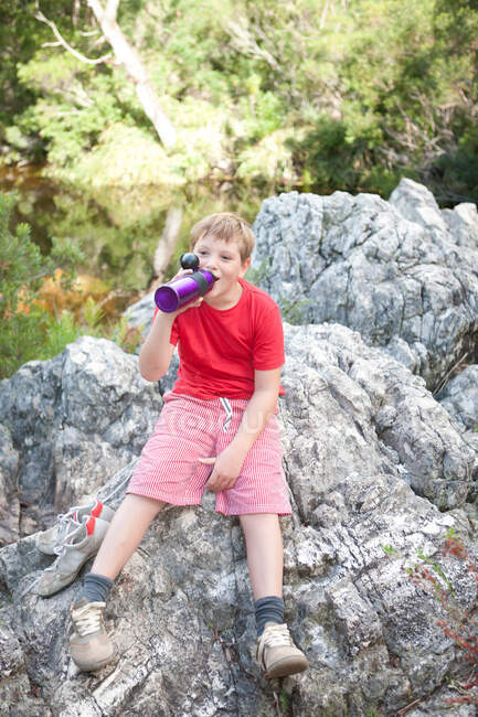 Retrato do menino bebendo do frasco na rocha — Fotografia de Stock