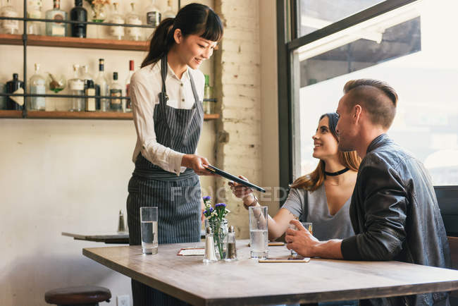 Kellnerin überreicht jungen Pärchen Rechnung in Restaurant — Stockfoto