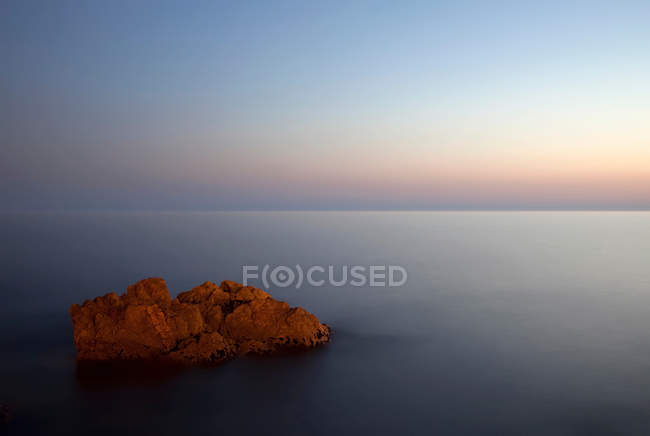 Довгий експозиційний знімок каменю в морі на заході сонця — стокове фото