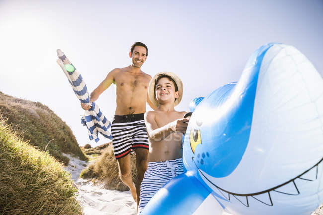 Boy and father running down sand dune carrying shark inflatable, Cape Town, South Africa — Stock Photo