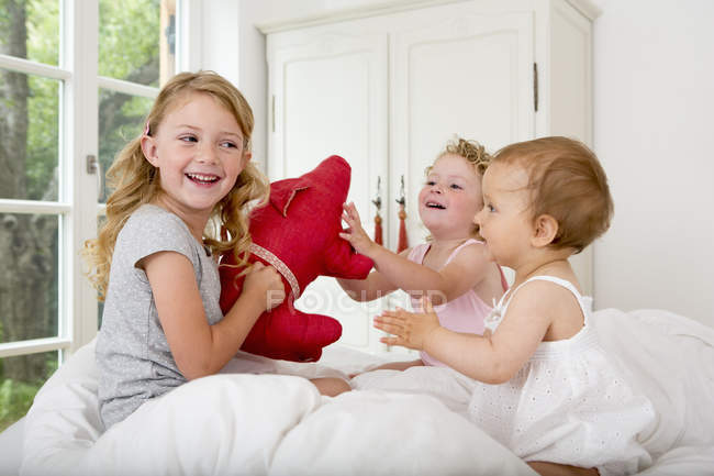 Три дівчини грають на ліжку з м'якою іграшкою — стокове фото