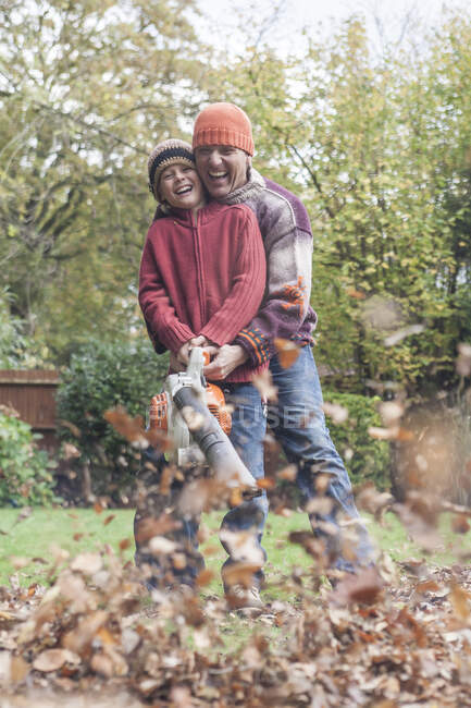 Padre e hijo usando el golpe de la hoja para despejar las hojas de otoño, riendo - foto de stock