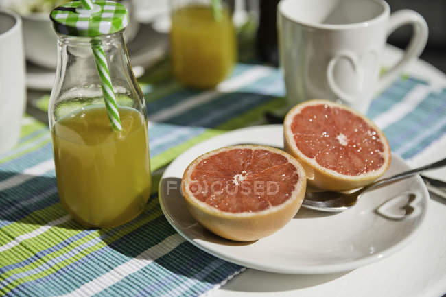 Toronja a la mitad y botella de jugo de naranja en la mesa - foto de stock