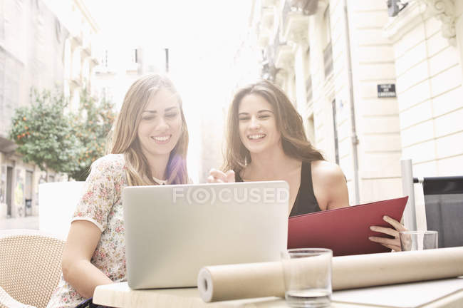 Две юные подруги смотрят на ноутбук в кафе на тротуаре, Валенсия, Испания — стоковое фото