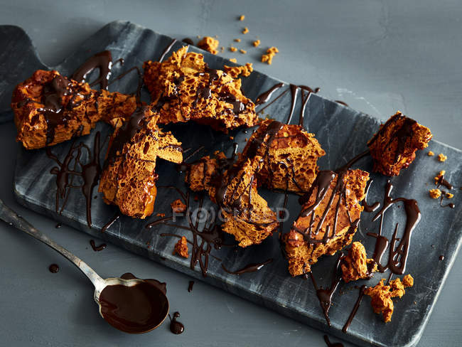 Broken honeycomb toffee with melted chocolate garnish on marble cutting board — Stock Photo