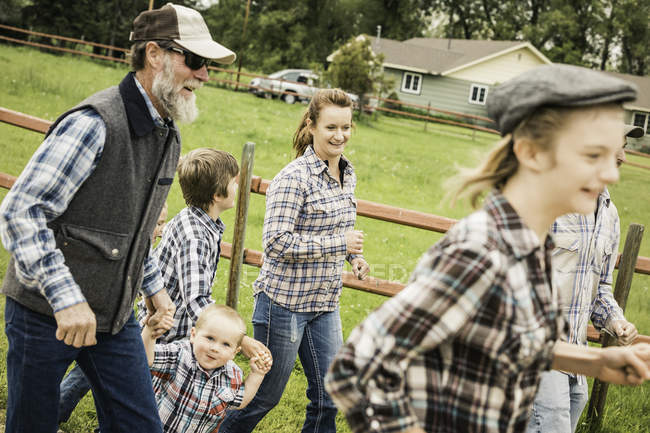 Вид сбоку семьи из нескольких поколений в футболках, бегущей по ферме и улыбающейся — стоковое фото