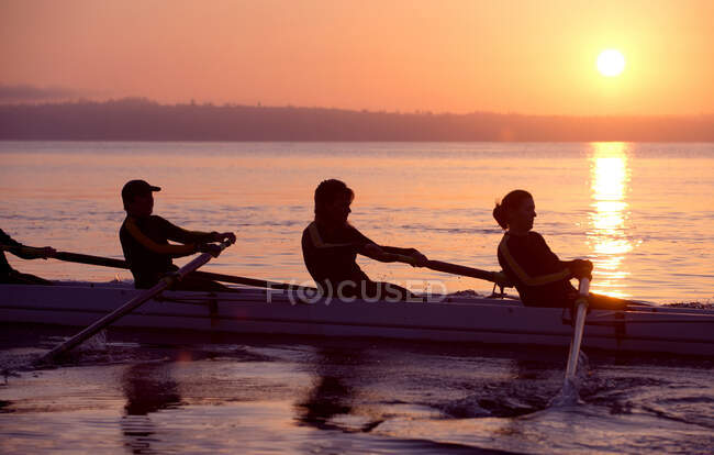 Quatre personnes ramant au coucher du soleil — Photo de stock
