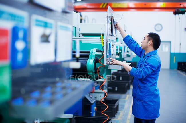 Trabajador en la fábrica de fabricación de piezas pequeñas en China, alcanzando hasta pulsar el botón en el panel de control - foto de stock