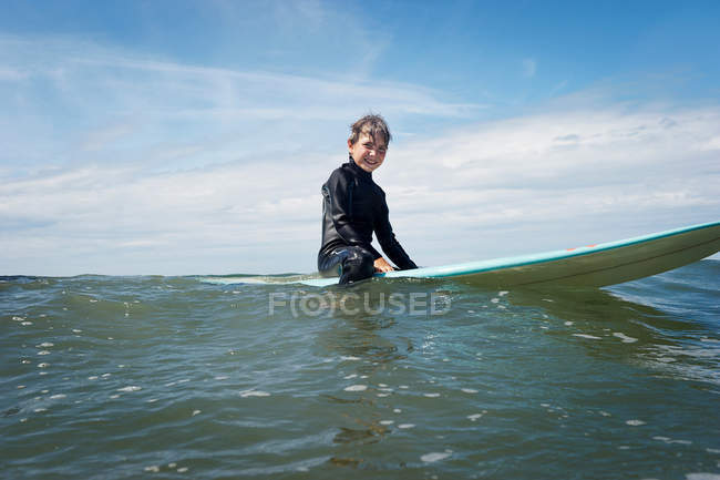 Мальчик сидит на доске для серфинга в море — стоковое фото