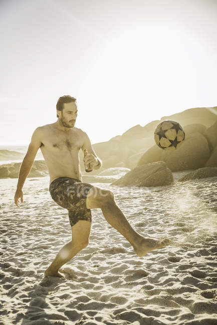 Uomo adulto che indossa pantaloncini da bagno e gioca a calcio sulla spiaggia, Città del Capo, Sud Africa — Foto stock