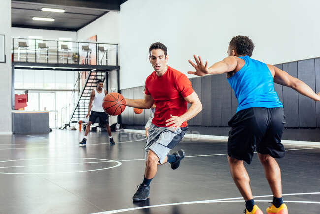 Dois jogadores de basquete do sexo masculino praticando corrida e defendendo bola na quadra de basquete — Fotografia de Stock