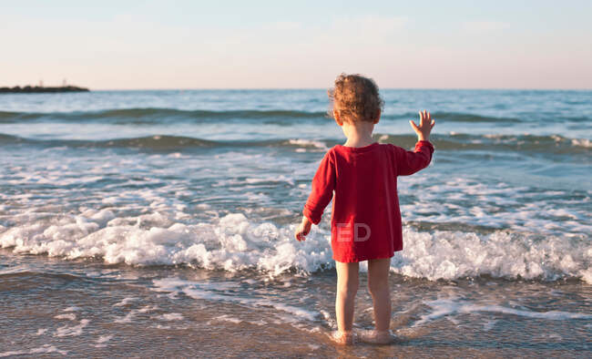 Menina criança de pé em ondas na praia — Fotografia de Stock