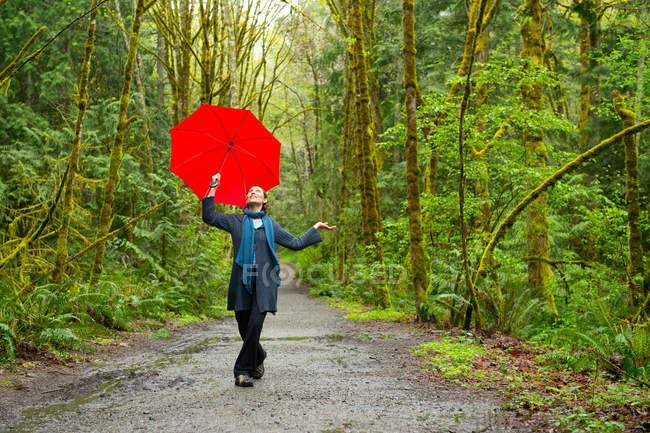 Femme sur le sentier forestier avec parapluie rouge — Photo de stock