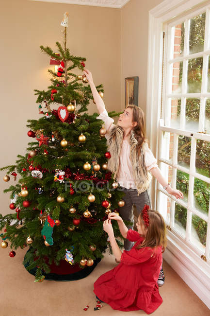 Chica con hermana decorando árbol de Navidad - foto de stock