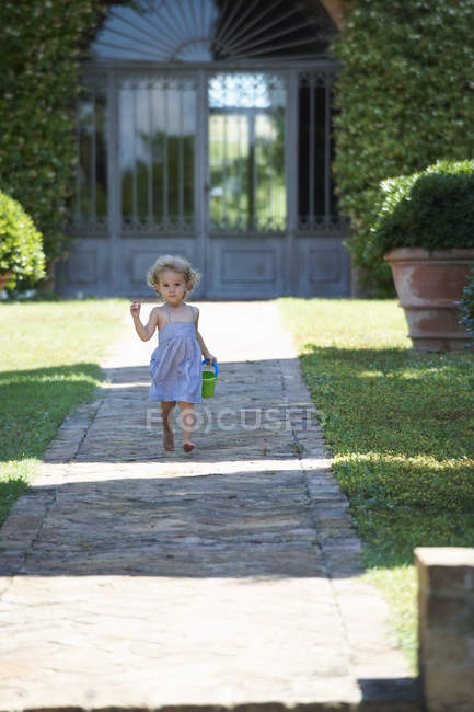 Girl running through garden carrying bucket — Stock Photo