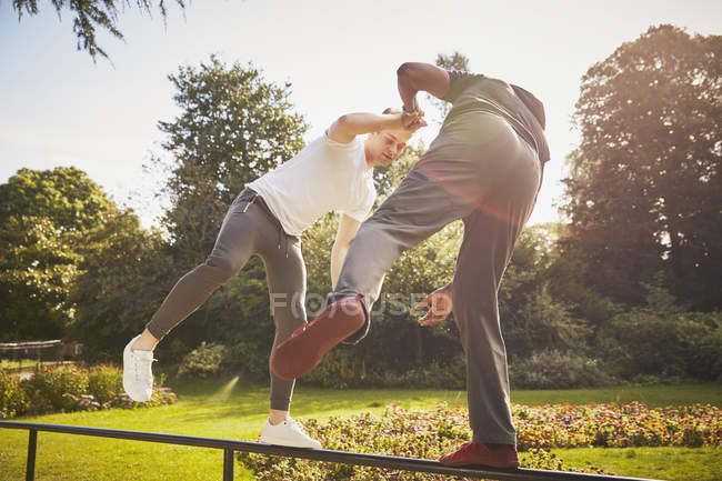 Uomo che si tiene per mano con personal trainer bilanciamento su una gamba sulla recinzione del parco — Foto stock