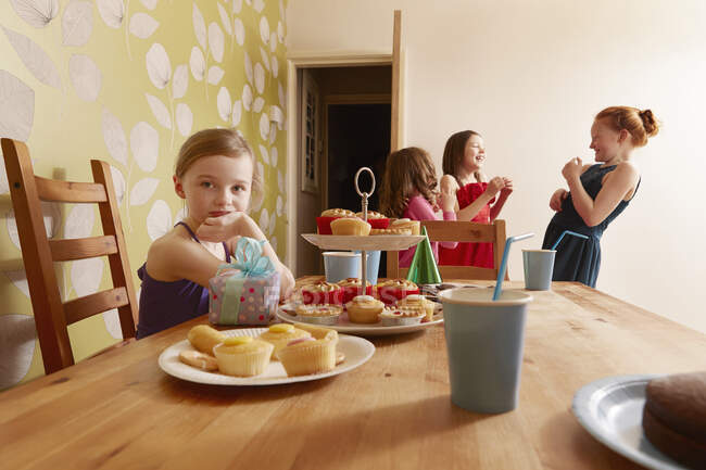 Дівчина за столом з партійною їжею, друзі на задньому плані — стокове фото