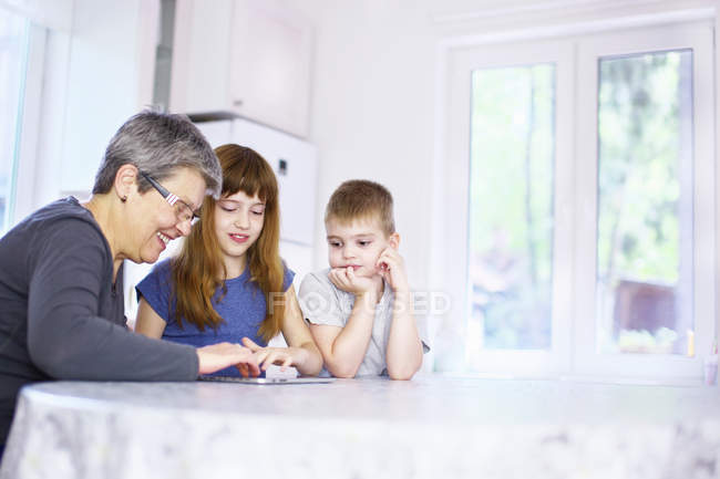 Abuela y nietos usando tableta digital en la mesa de la cocina - foto de stock