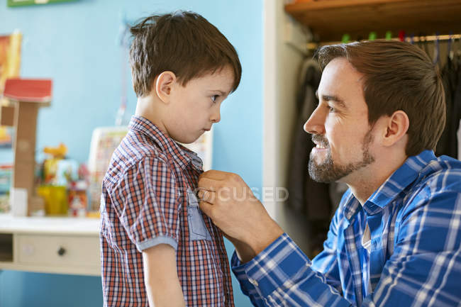 Father helping son button shirt in bedroom — Stock Photo