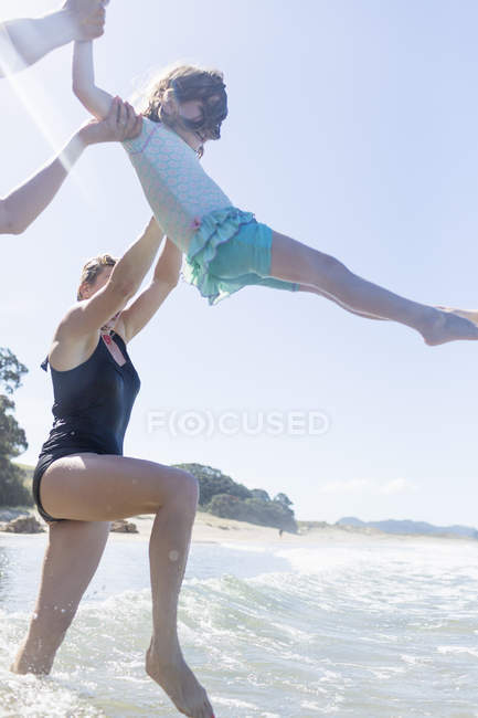 Dos mujeres levantando chicas sobre las olas del océano, Playa de Agua Caliente, Bahía de las Islas, Nueva Zelanda - foto de stock