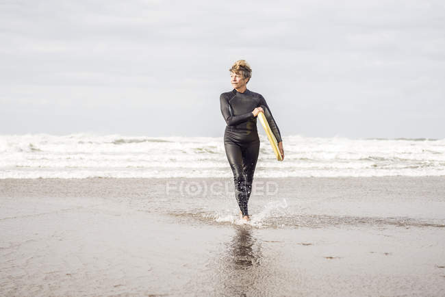 Mature female bodyboarder paddling on Devon coast, UK — Stock Photo