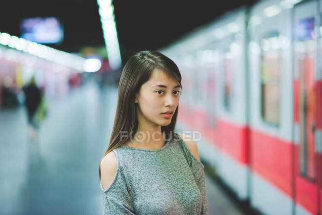 Mujer joven esperando tren en la plataforma ferroviaria por la noche - foto de stock