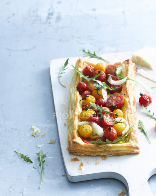 Tomato and parmesan puff pastry tart garnished with rocket on cutting board — Stock Photo