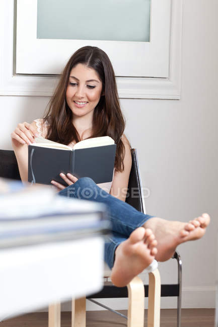 Giovane donna adulta lettura libro con i piedi in su — Foto stock