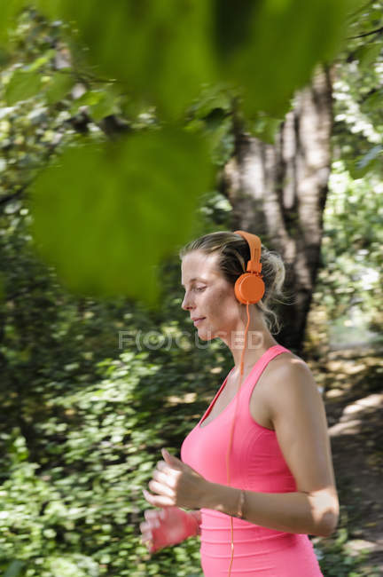 Jovem mulher correndo através do parque arborizado — Fotografia de Stock