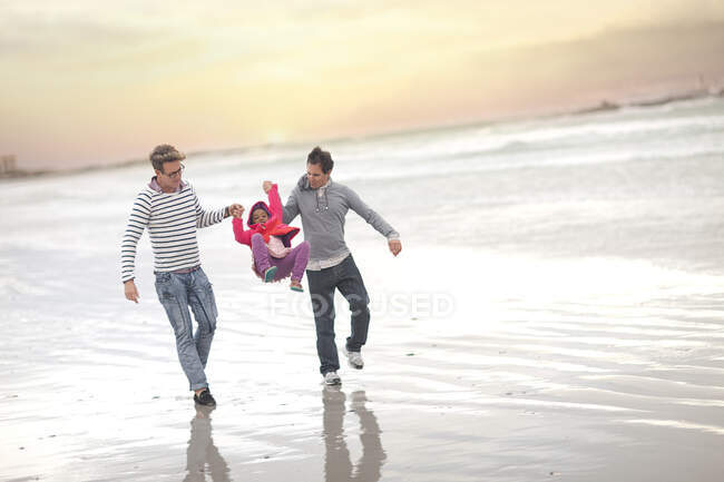 Gay couple swinging child on beach — Stock Photo